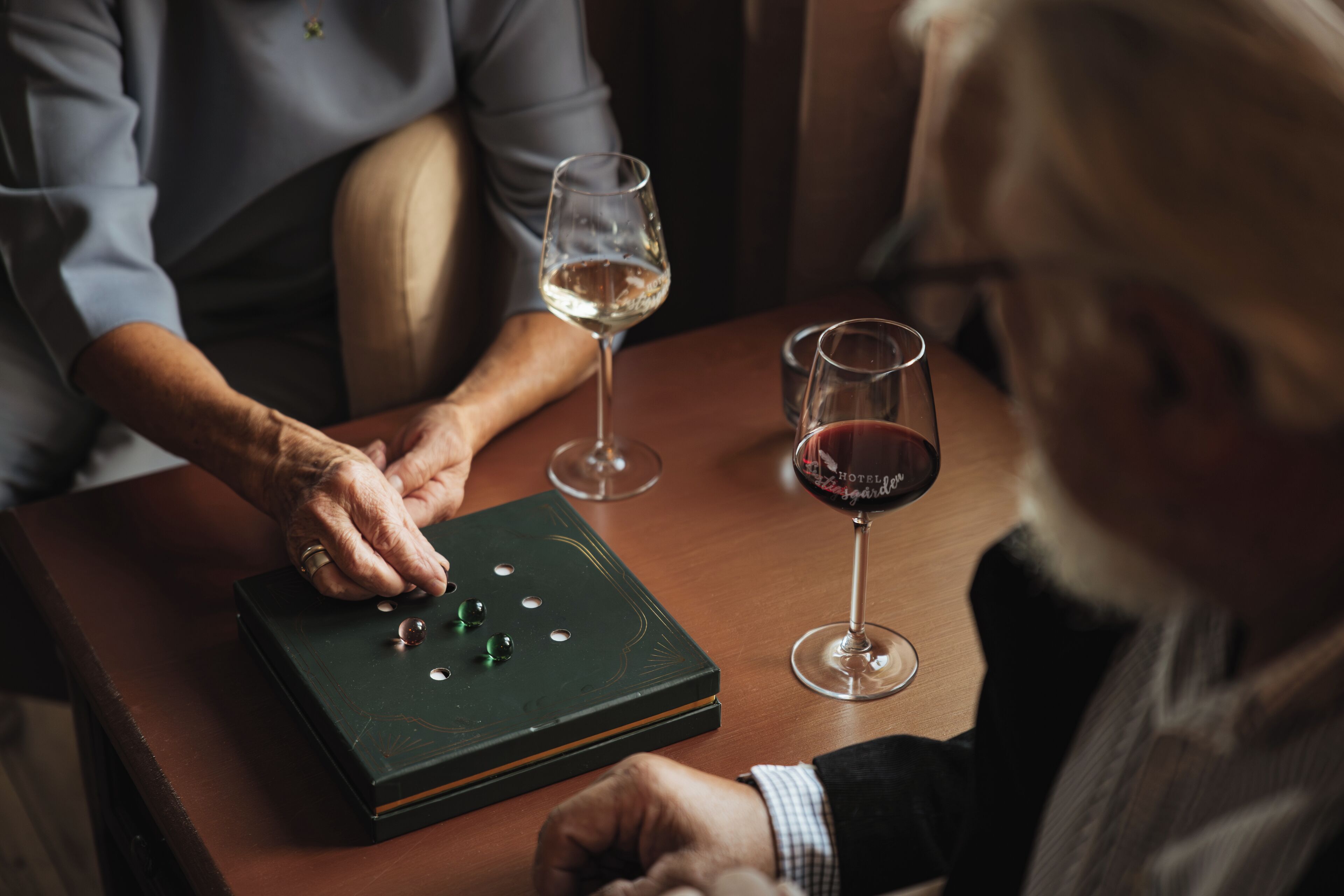 A person playing a game of dominoes on a wooden table with two glasses of wine.