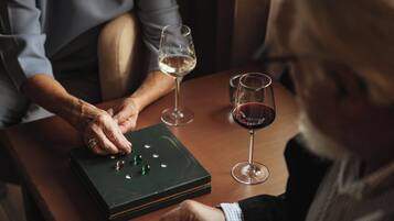 A person playing a game of dominoes on a wooden table with two glasses of wine.