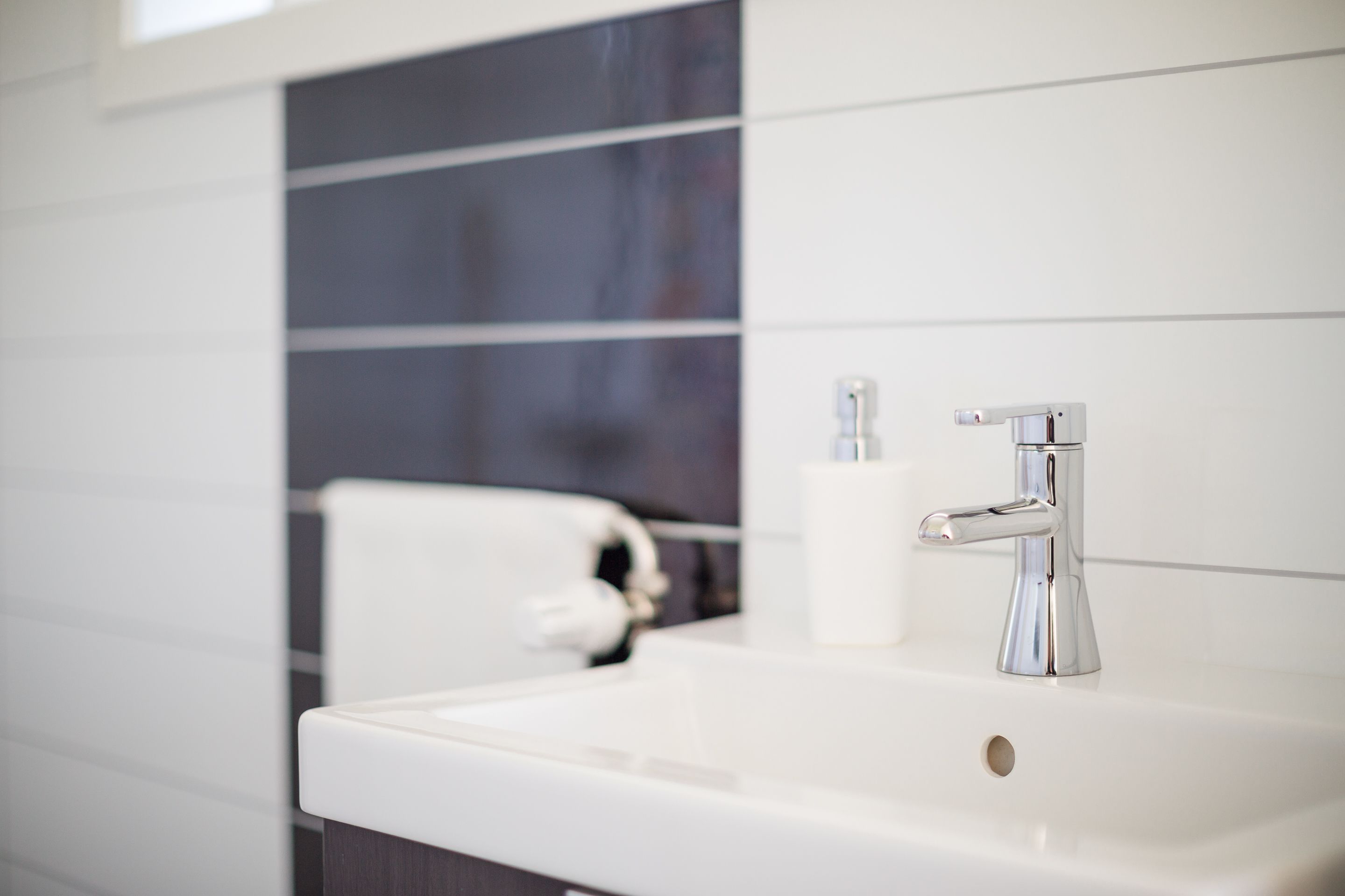 A modern bathroom with a white sink, chrome faucet, and a toilet.