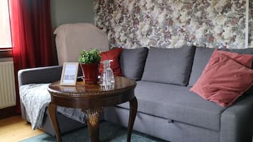 Una sala de estar con un sofá gris, una mesita de madera con un código QR, una planta en maceta y un papel tapiz floral.
