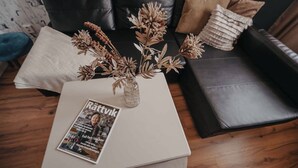Un salon avec une table basse blanche, un magazine et un vase contenant des plantes séchées.