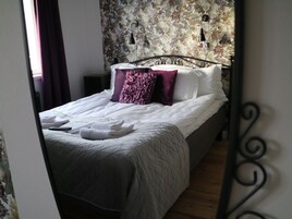 Una cama bien hecha con sábanas blancas y una colcha gris acolchada, una almohada morada y una almohada blanca.