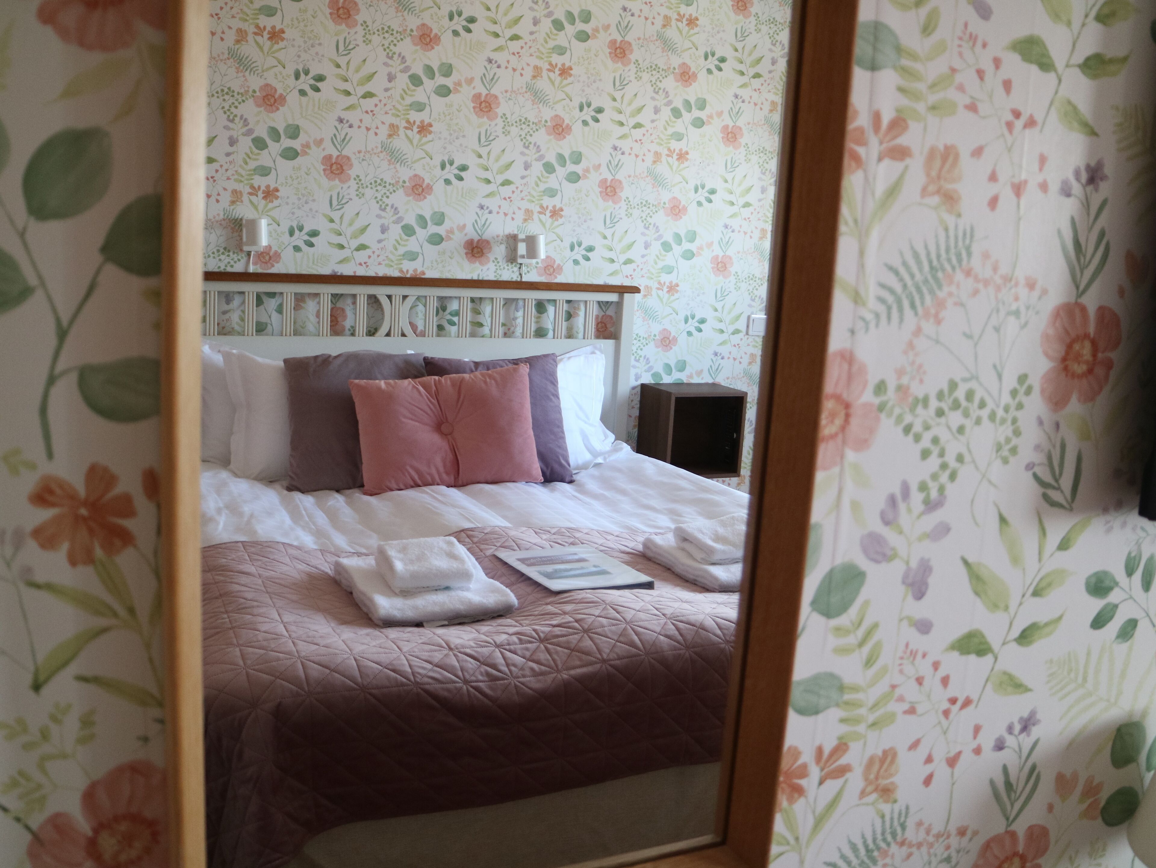 A neatly made bed with a pink and white quilt, pillows, and folded towels.