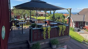 Un espace extérieur aménagé, abrité et doté de tables et de chaises, entouré d’une terrasse en bois et offrant une vue sur un lac.