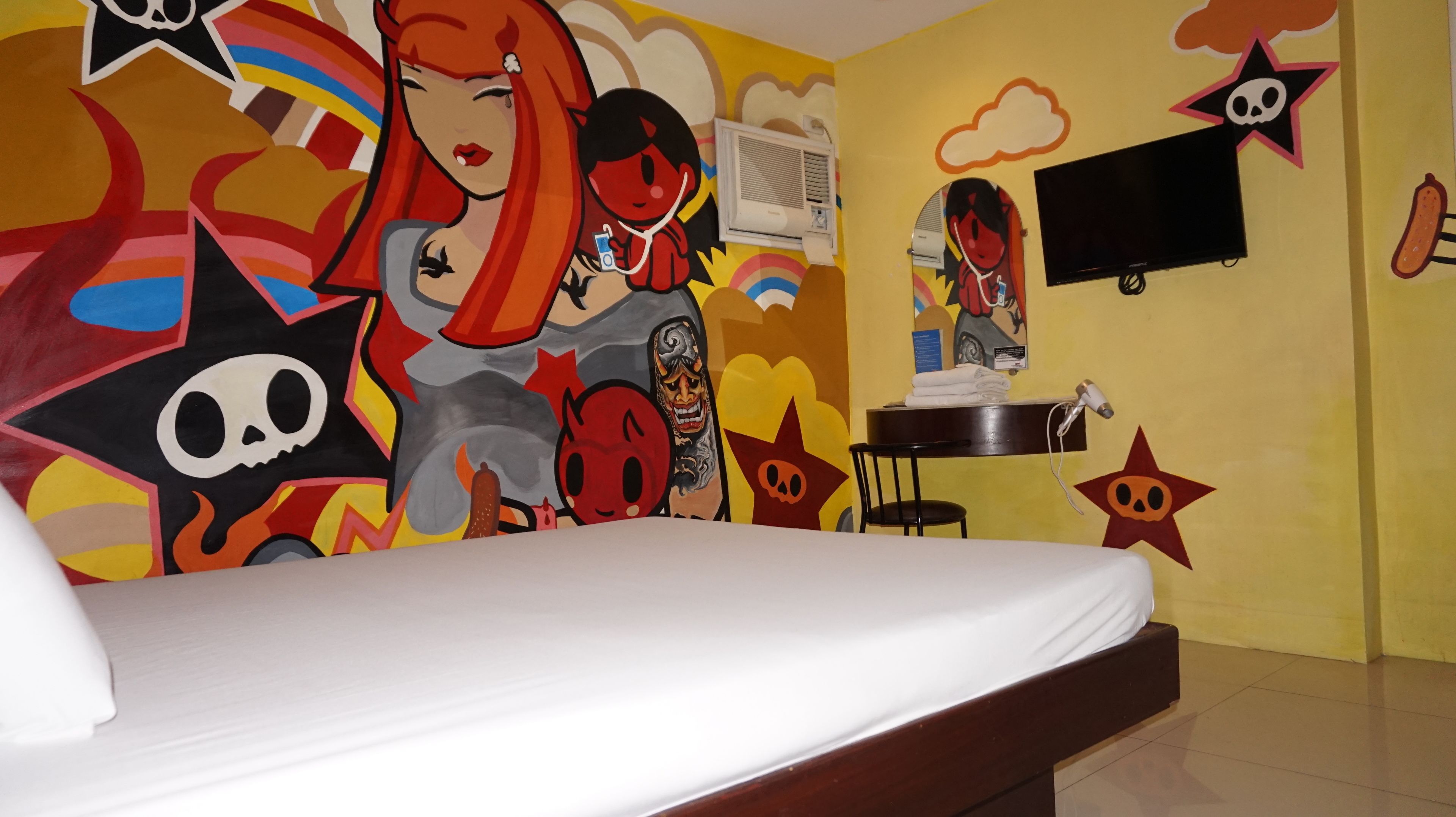 A room with a bed, a desk, and a wall with colorful murals.