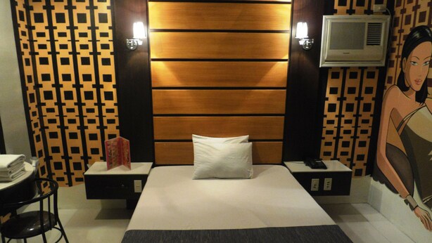 Een hotelkamer met een bed, een bureau en een stoel. Er is een muur met een patroon en een schilderij aan de muur.