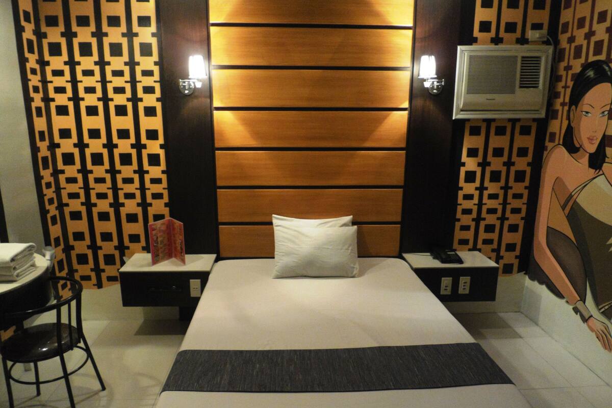 Een hotelkamer met een bed, een bureau en een stoel. Er is een muur met een patroon en een schilderij aan de muur.