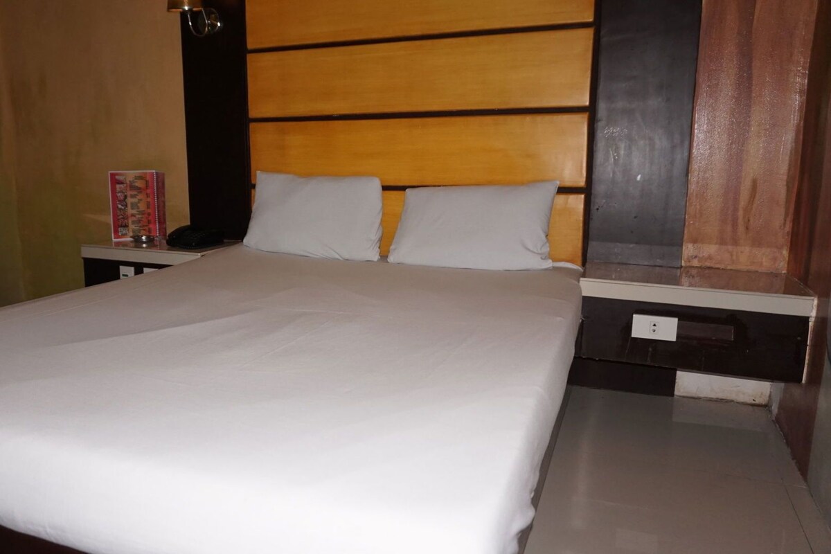 Une chambre d’hôtel avec un grand lit, une tête de lit en bois, une table de chevet avec une lampe et une petite table avec un téléphone.
