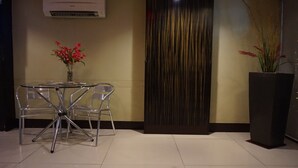 Een moderne kamer met een tafel met glazen blad en metalen stoelen, een donker gordijn en een kamerplant.