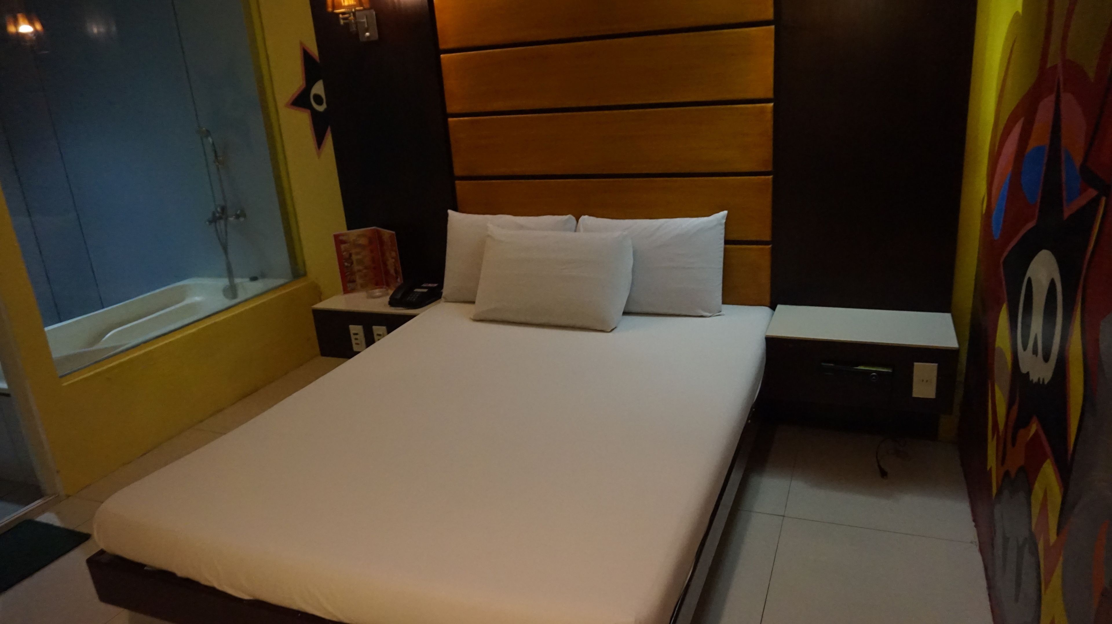 Una habitación de hotel con una cama, mesitas de noche, un ventanal y una puerta.