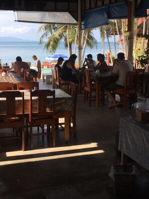 An outdoor dining area with wooden tables and chairs, umbrellas, and a view of the ocean. - Starlight Haad Rin Resort (Ko Pha-ngan)