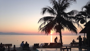 Un espai relaxant a la platja amb gandules i una palmera, amb vista al mar tranquil al capvespre.