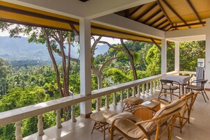 A covered outdoor seating area with wicker furniture and a table, overlooking a lush green landscape.