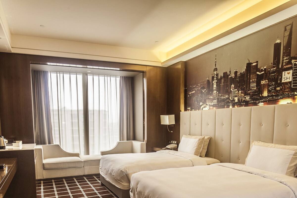 Een hotelkamer met twee bedden, een bank, een bureau en een groot raam met gordijnen.