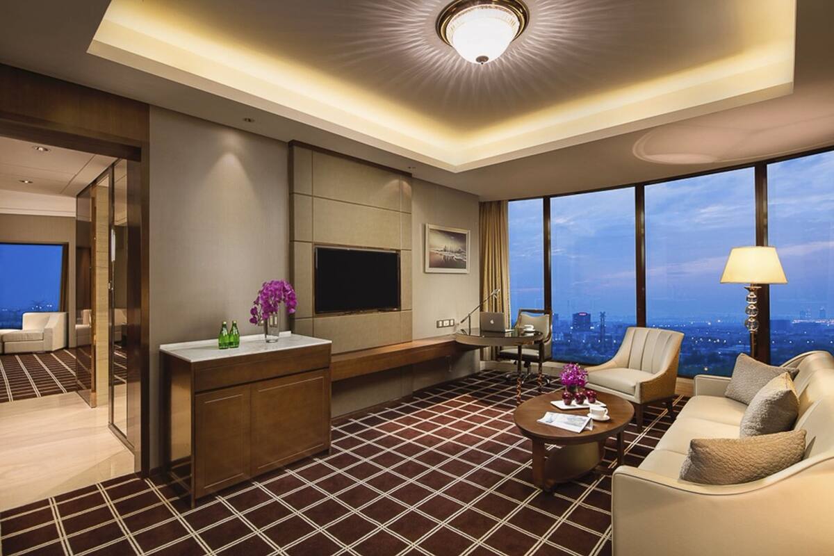 Een moderne hotelkamer met een groot raam met uitzicht over de stad, een flatscreen televisie, een bureau met stoel en een bank.