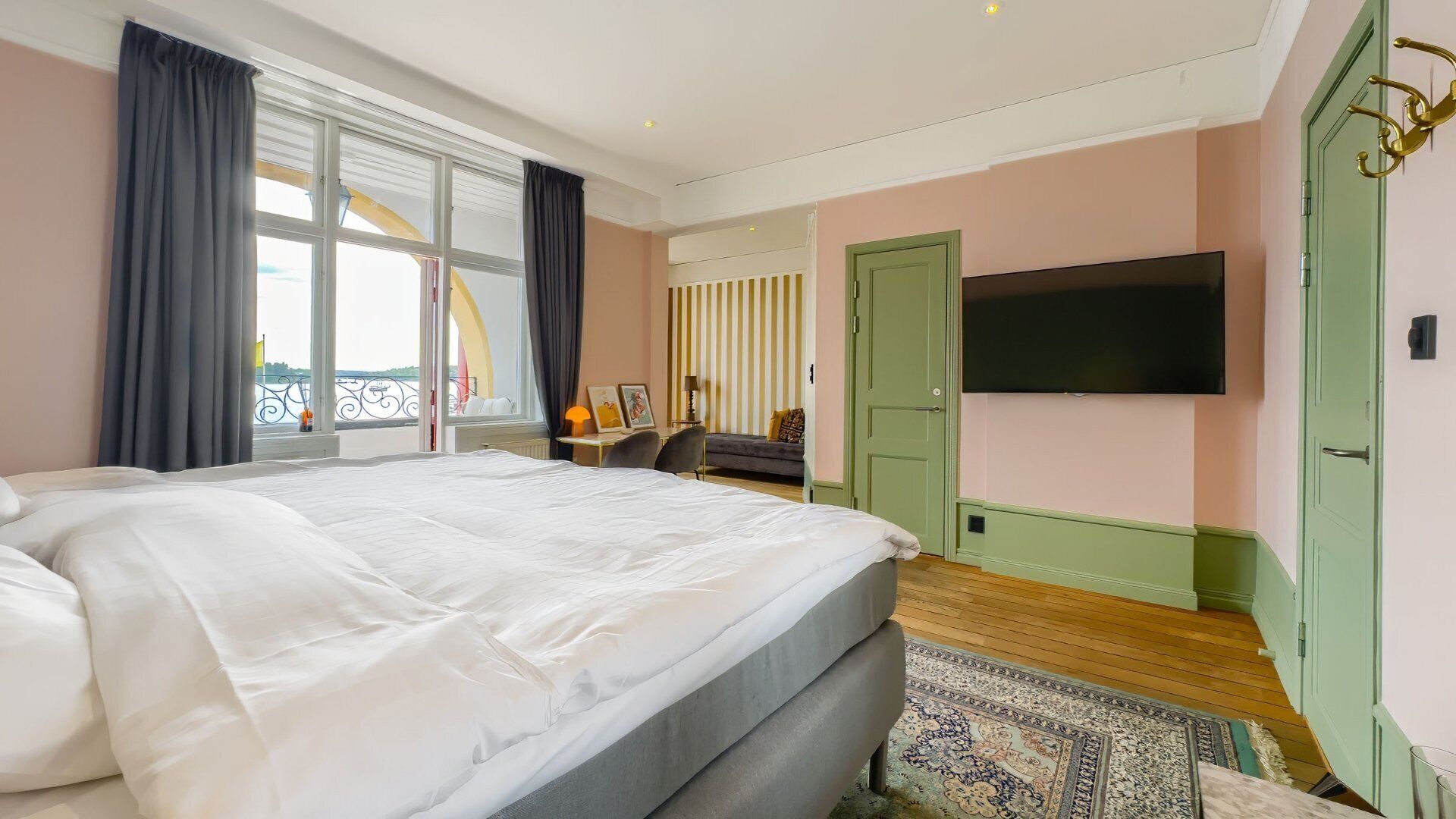 A bedroom with a large bed, a TV mounted on the wall, and a view of the outside balcony.