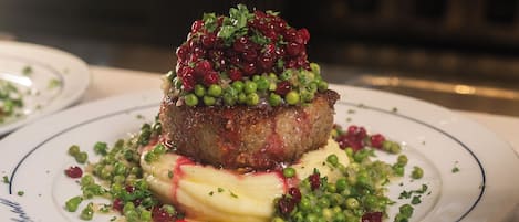 Un plato con un guiso de carne como pieza central, adornado con guisantes y hierbas, sobre un plato blanco con un borde azul.