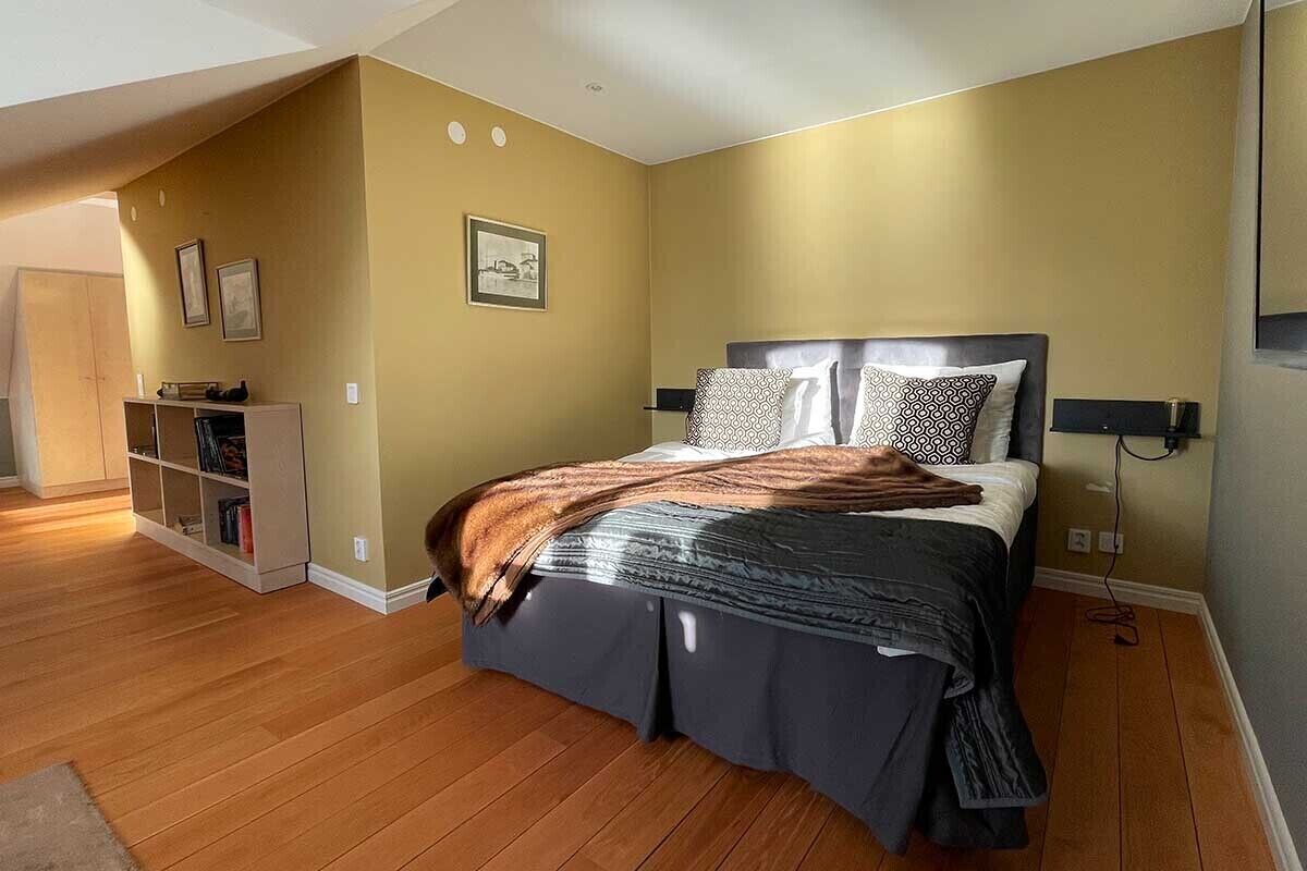 A bedroom with a bed, wooden flooring, a bookshelf, and a framed picture on the wall.
