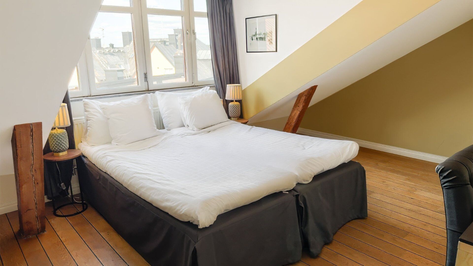 A bedroom with a large bed, a window with curtains, a lamp, and a picture on the wall.