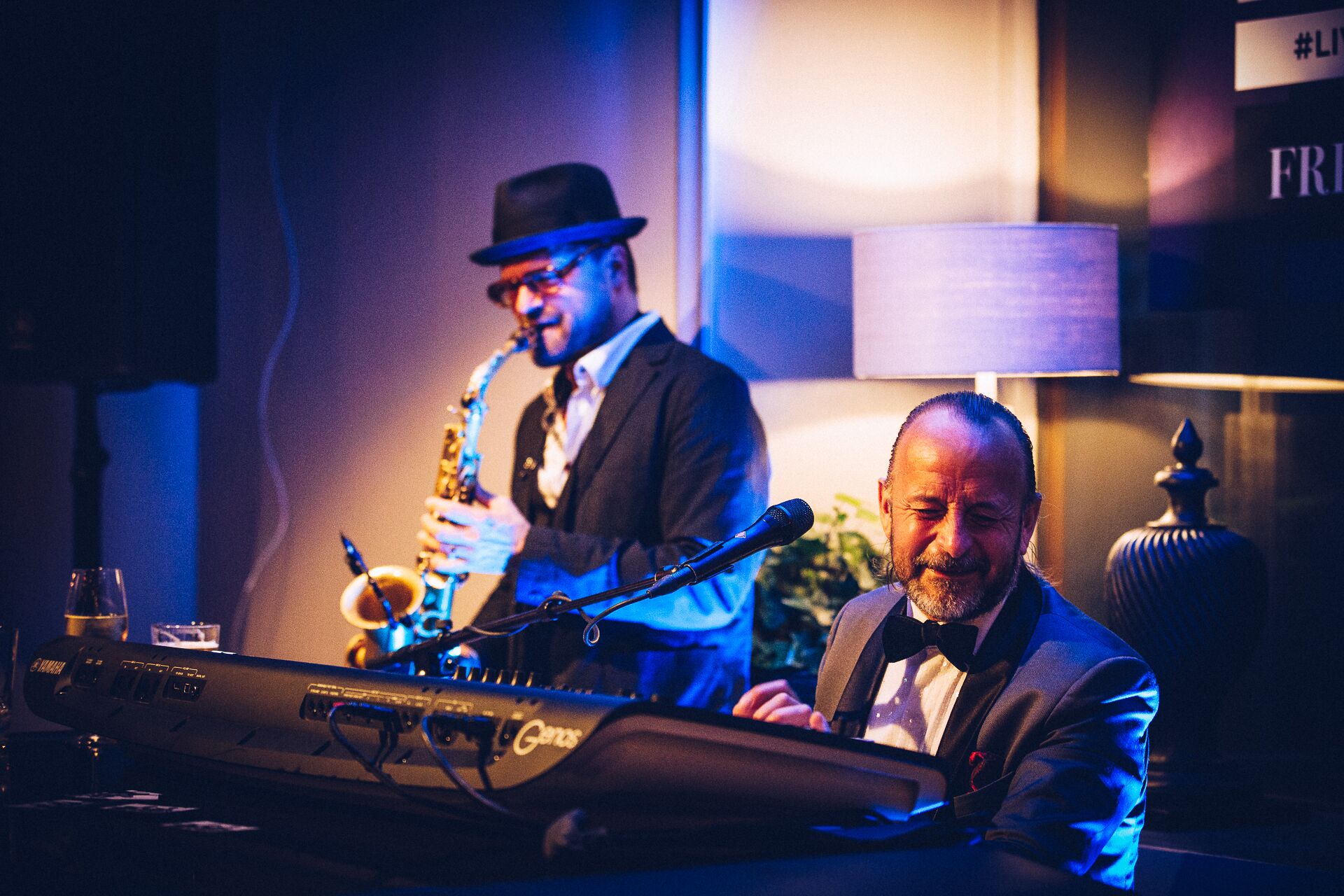 Una band jazz che si esibisce con una tastiera e un sassofono, un microfono e una lampada sullo sfondo.