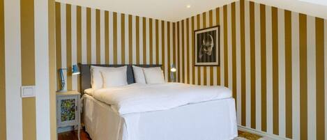 Un dormitorio con una cama, una mesita de noche, una lámpara de pared y una alfombra a cuadros.