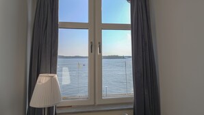 A room with a large window overlooking a body of water, a lamp, and a chair.
