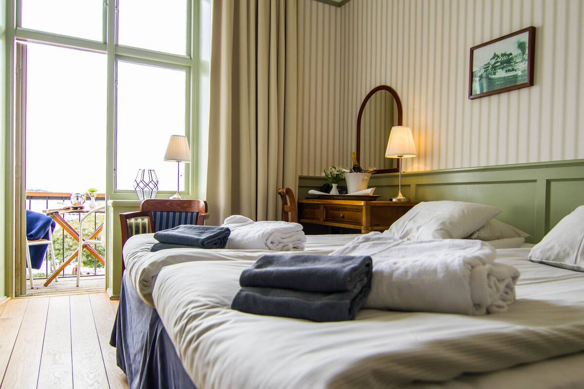 A hotel room with a large bed, a desk with a lamp, a chair, and a view of the outdoors through a window.
