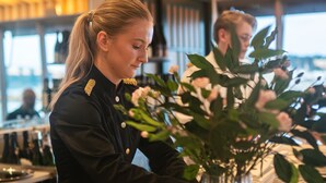 A bar area with a person in uniform, a vase with flowers, and a patterned tablecloth.