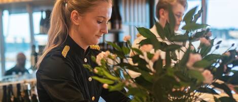 A bar area with a person in uniform, a vase with flowers, and a patterned tablecloth.