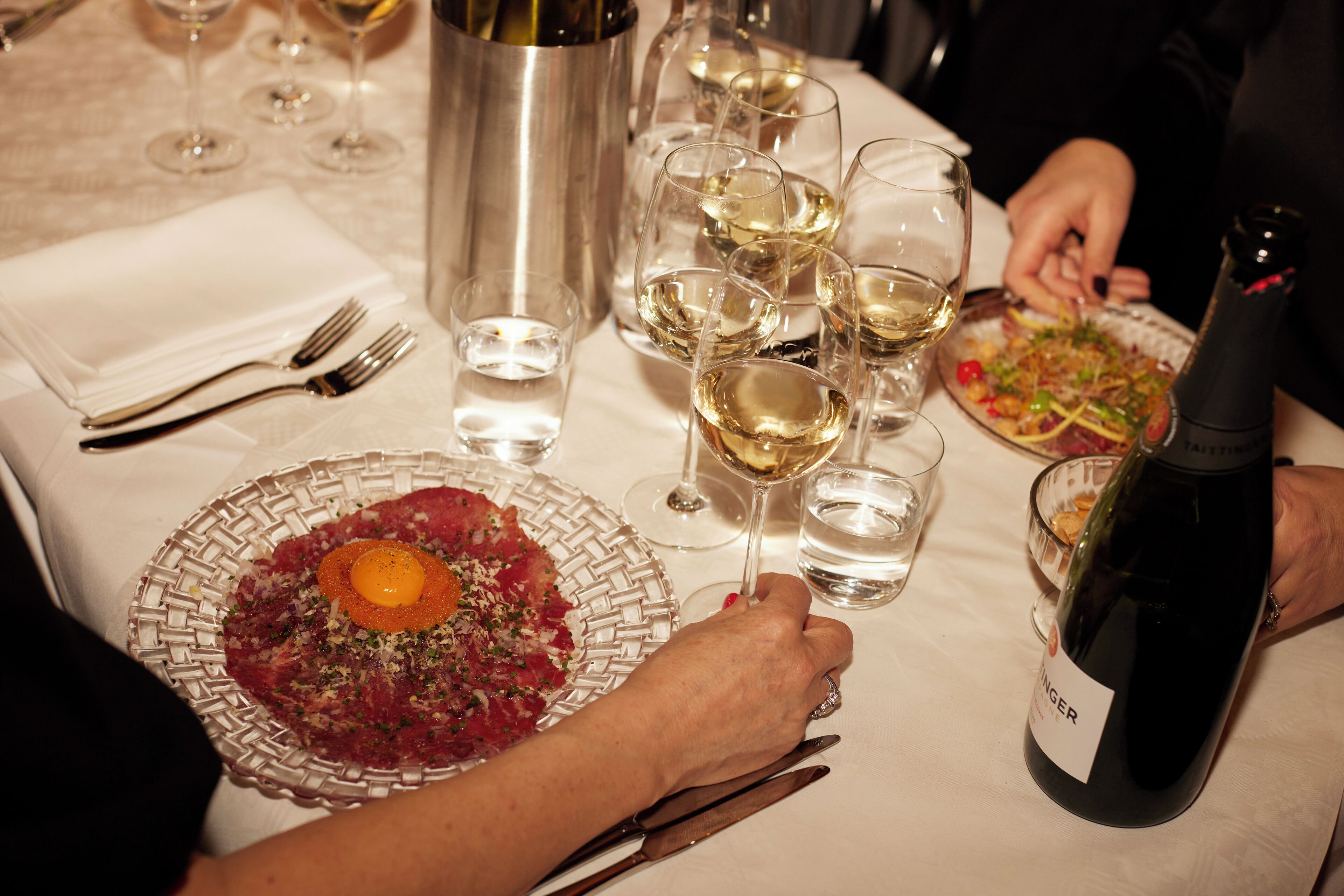 A dining table with plates of food, wine glasses, and a bottle of wine.