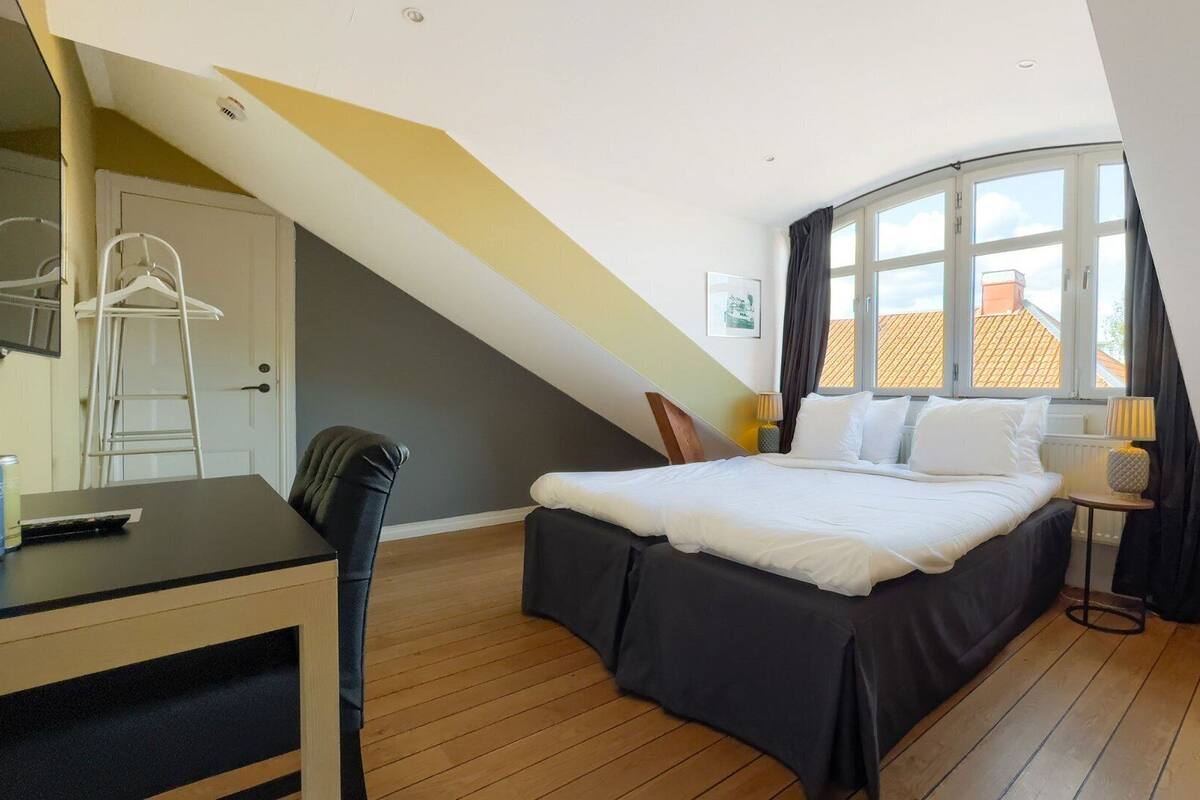 A bedroom with a bed, a desk, a chair, and a window with curtains.