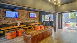 A modern interior with a brick wall, wooden tables, a leather sofa, and a TV mounted on the wall. - never at home Green Point (Cape Town)