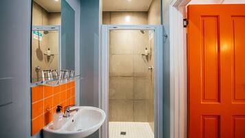 Une salle de bain avec un lavabo blanc, une douche dont le carrelage est orange et une porte d’un orange vif.