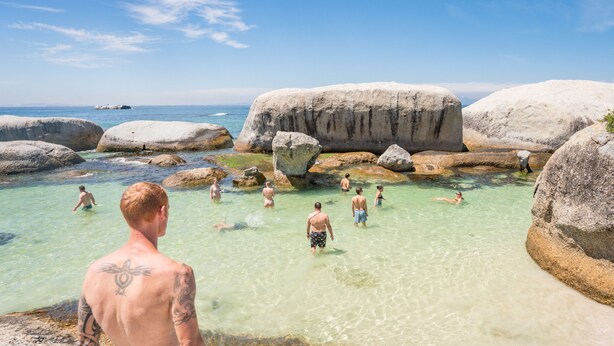 A clear, shallow pool surrounded by large rocks with people swimming and walking around. - never at home Green Point (Cape Town)