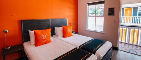 A hotel room with two beds, a nightstand, a lamp, and a window with a view of the outside.