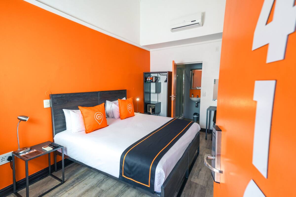 A hotel room with a large bed, orange walls, a modern design, and a visible bathroom.