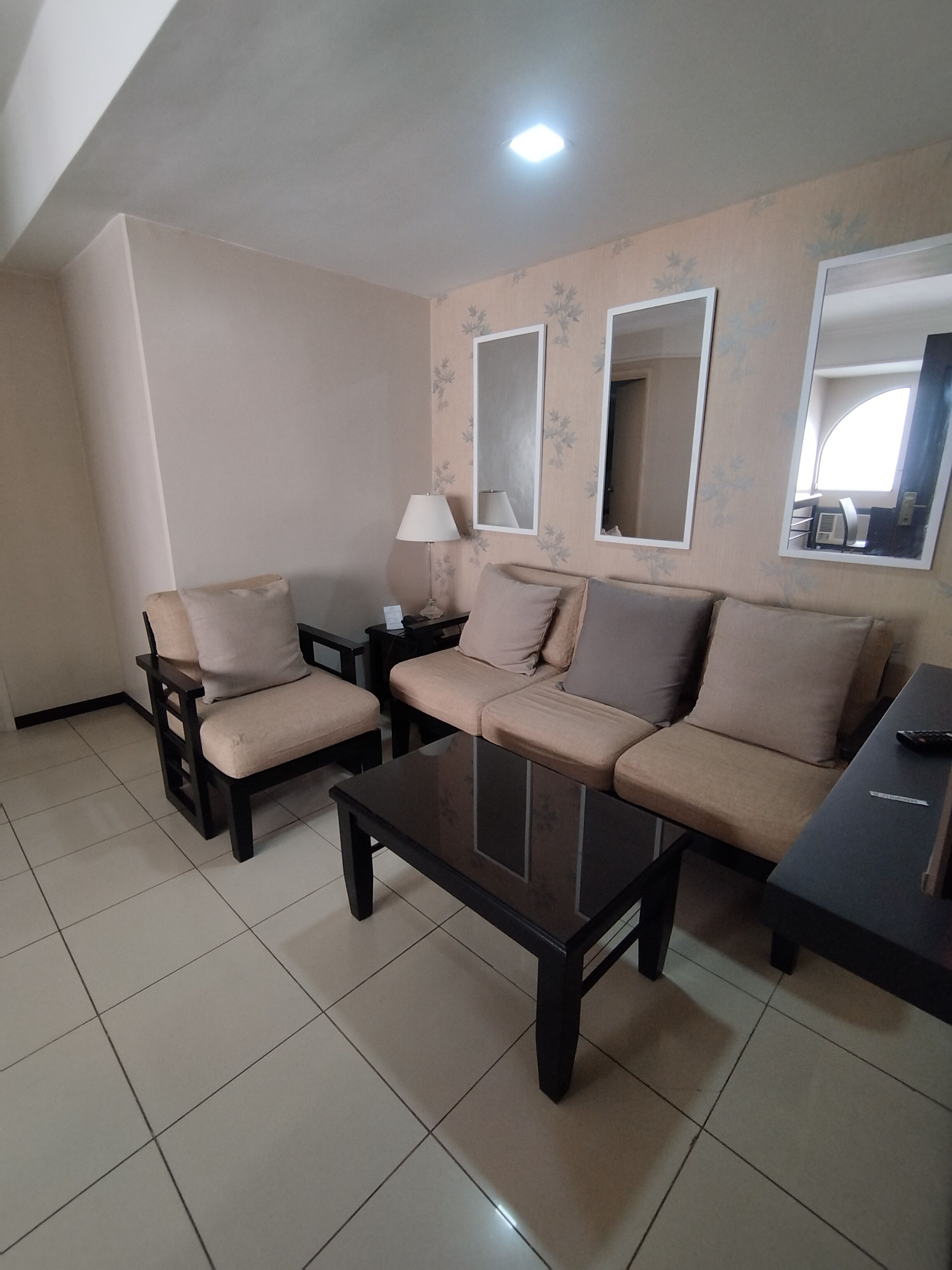 A living room with a sofa set, a coffee table, a lamp, and two wall mirrors.
