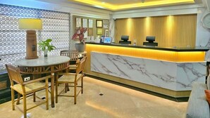 A hotel reception area with a marble counter, wooden chairs, a round table, and a potted plant. - Ralph Anthony Suites (Manila)