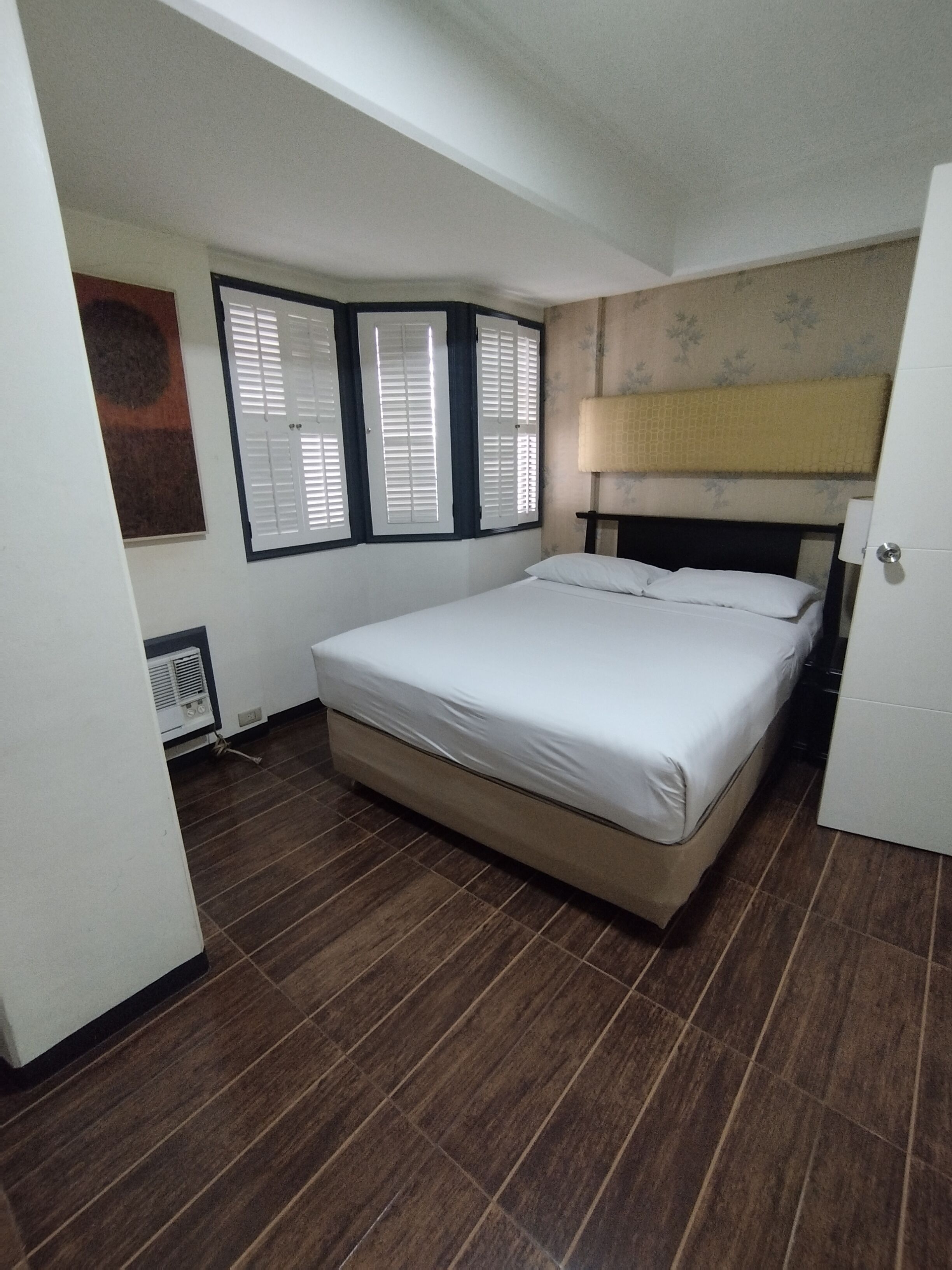 A bedroom with a bed, a radiator, and a window with shutters.