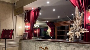 Um balcão de recepção de mármore com a marca 'Colbert Palace', cortinas vermelhas e uma planta decorativa.