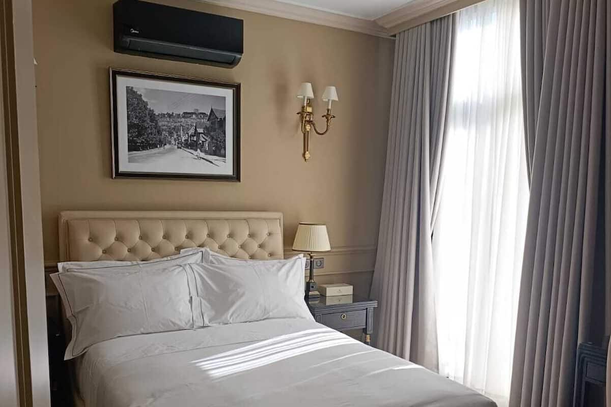 Ein Hotelzimmer mit einem großen Bett, einem gerahmten Bild an der Wand, einem Nachttisch mit Lampe und einem Fenster mit Vorhängen.
