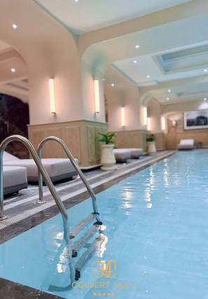 Una piscina con una escalera metálica, sillas de descanso y luces fijadas a la pared.