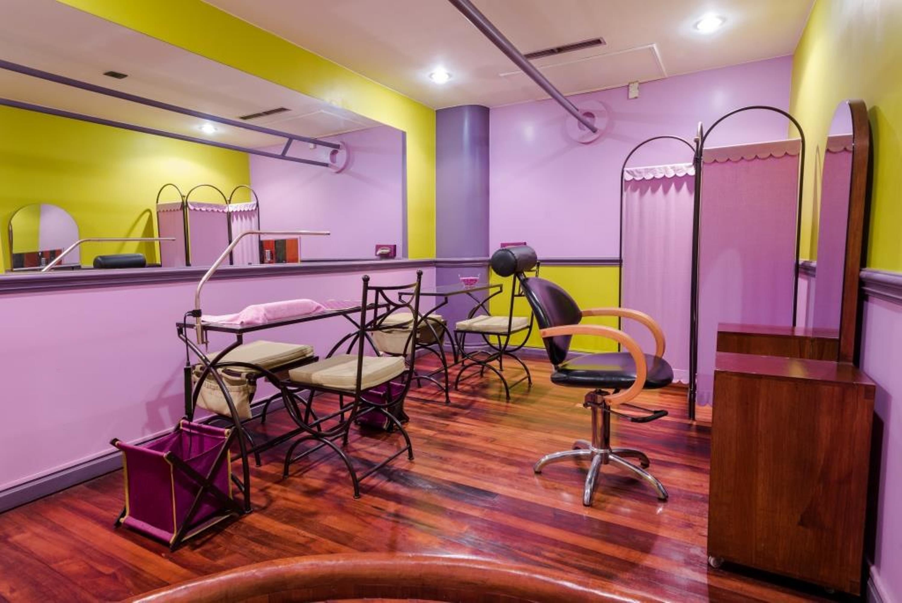 A room with a wooden floor, mirrored vanity, multiple chairs, and a wooden cabinet.