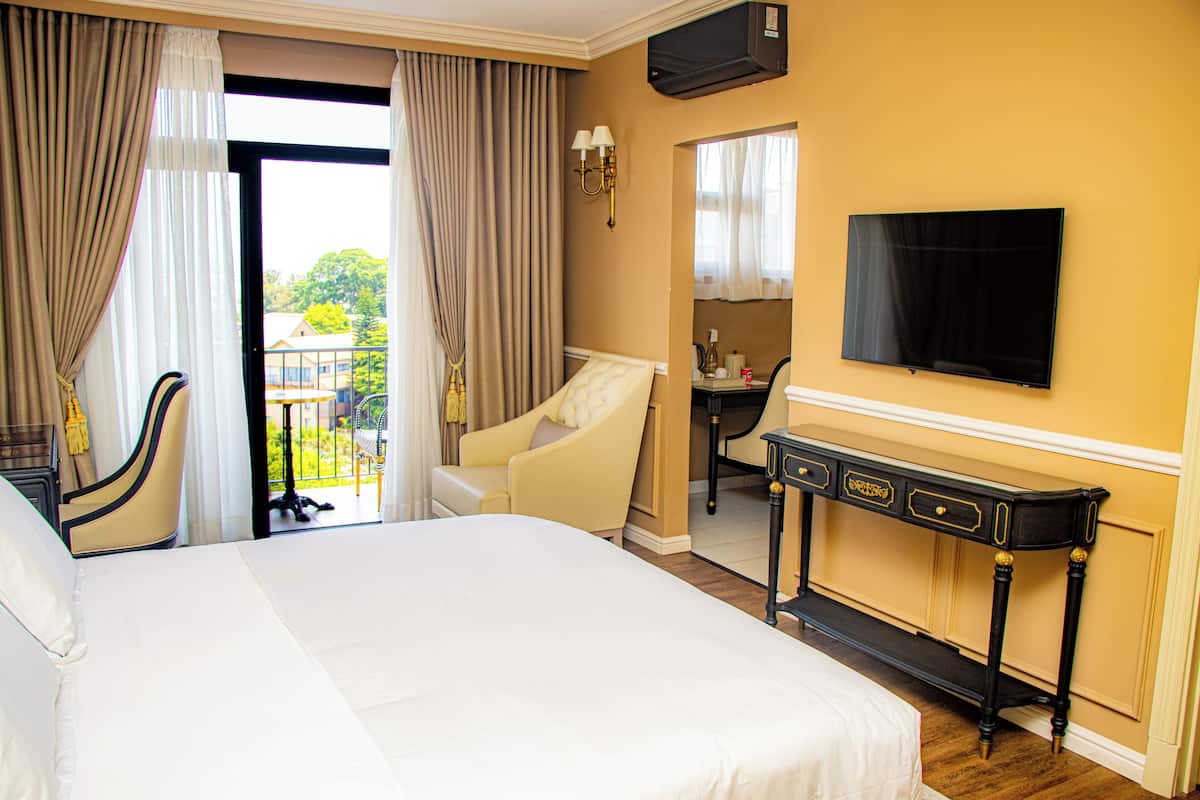 Ein Hotelzimmer mit einem großen Bett, einem Schreibtisch mit Stuhl, einem an der Wand befestigten Fernseher und Blick ins Freie durch ein Fenster.
