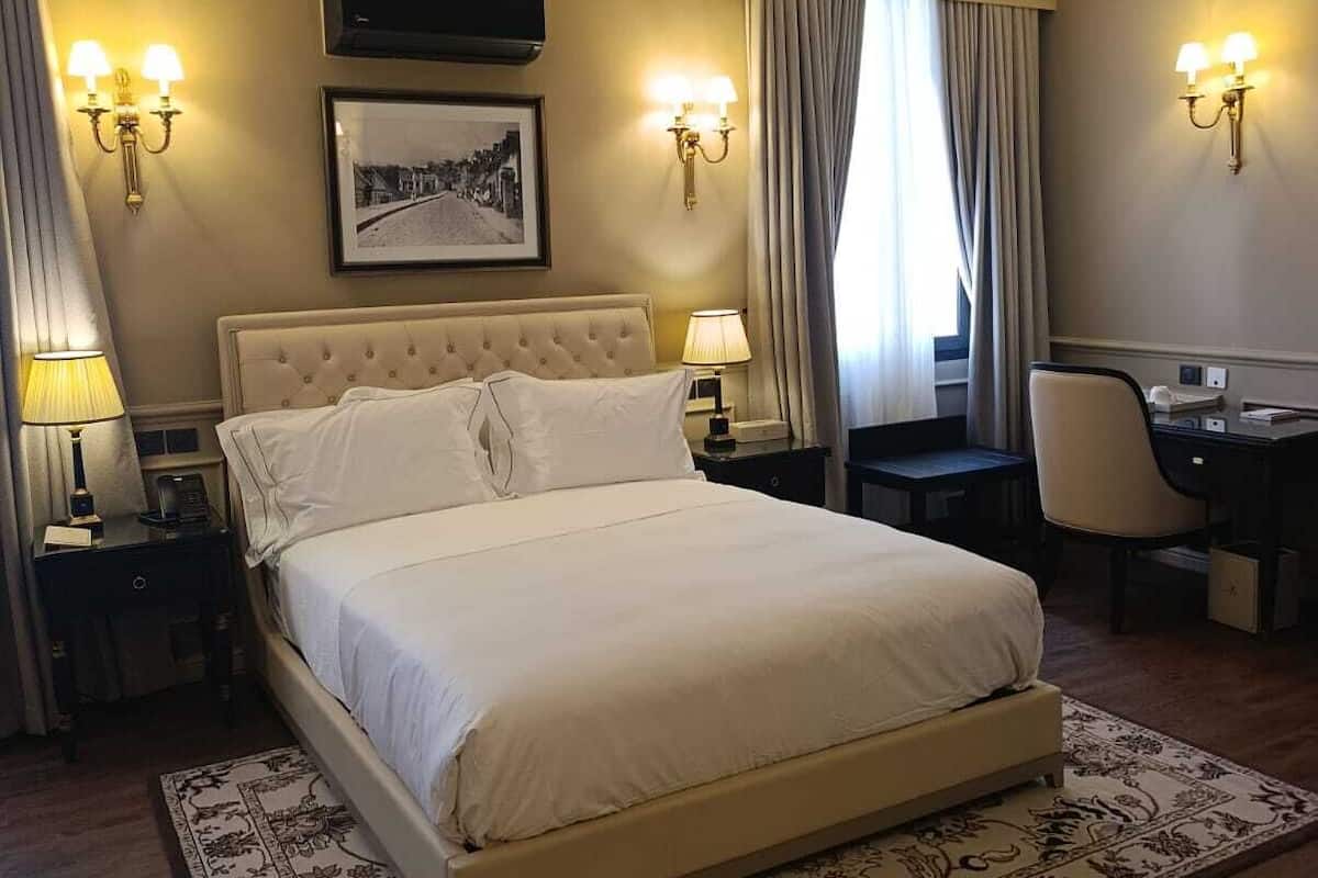 Ein Hotelzimmer mit einem großen Bett, zwei Nachttischen mit Lampen, einem Schreibtisch mit Stuhl und einem gerahmten Bild an der Wand.