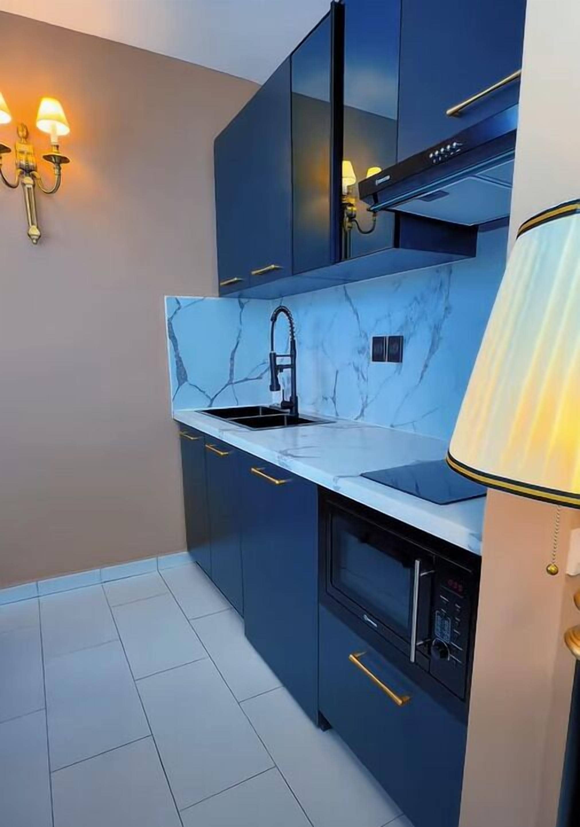 Una cocina moderna con gabinetes oscuros, encimera de mármol, horno empotrado y una lámpara fijada a la pared.
