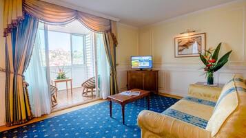 Una habitación con sofá, una mesita, televisor y ventana con cortinas.