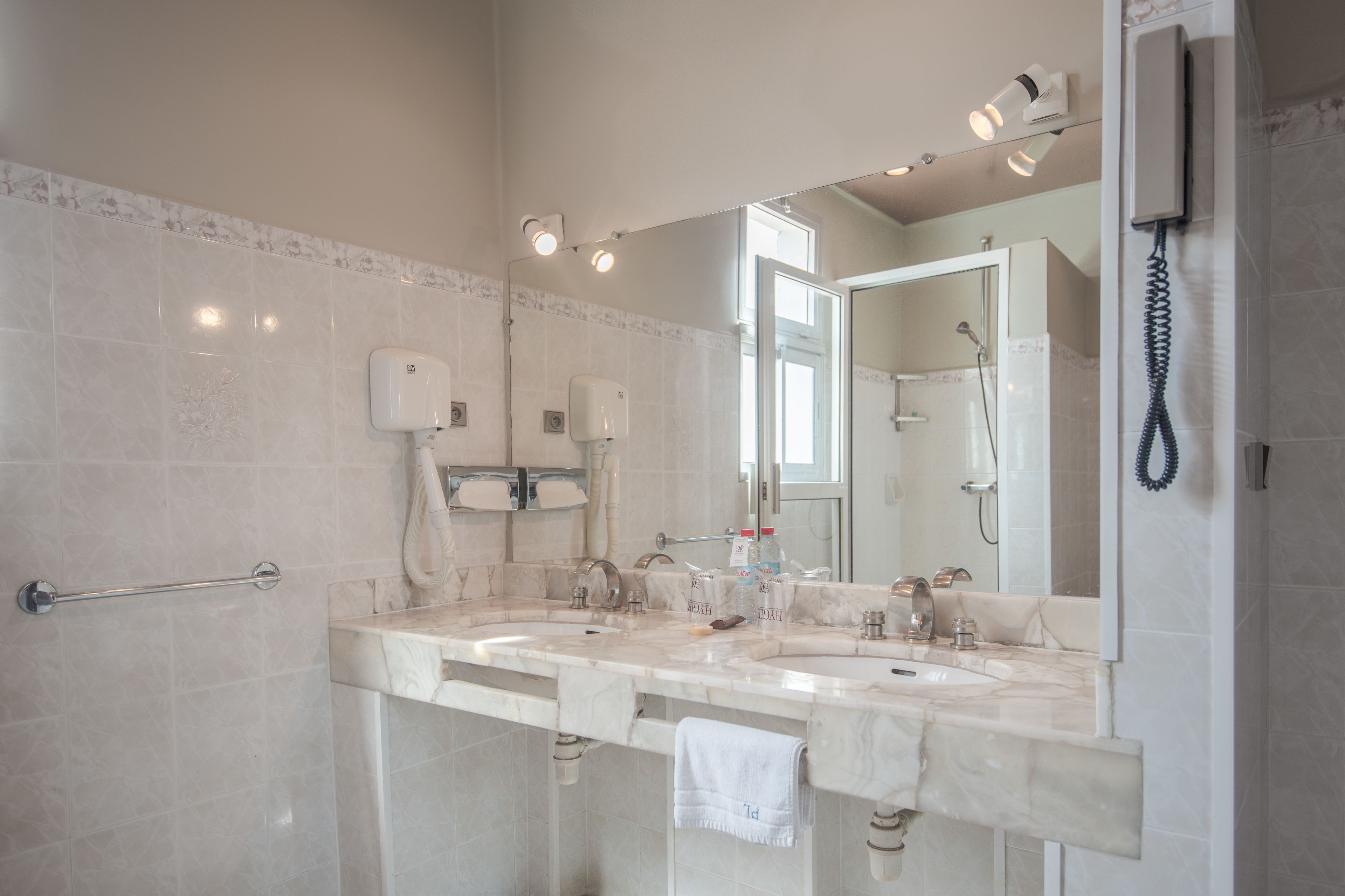 A bathroom with two sinks, a towel rack, a hand dryer, a mirror, and a shower.
