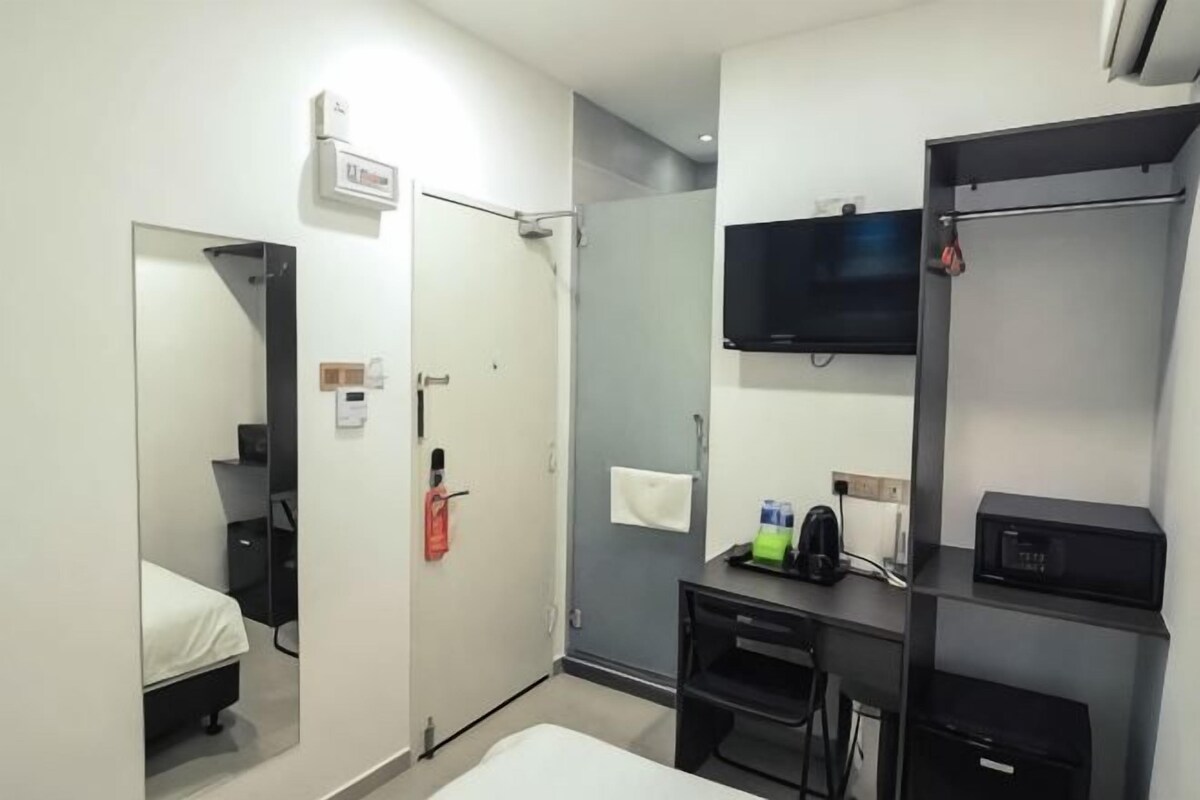 A hotel room with a bed, a desk, a TV, a shower, and a wardrobe.