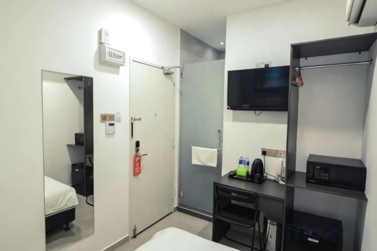 A hotel room with a bed, a desk with a chair, a television, and a wardrobe.